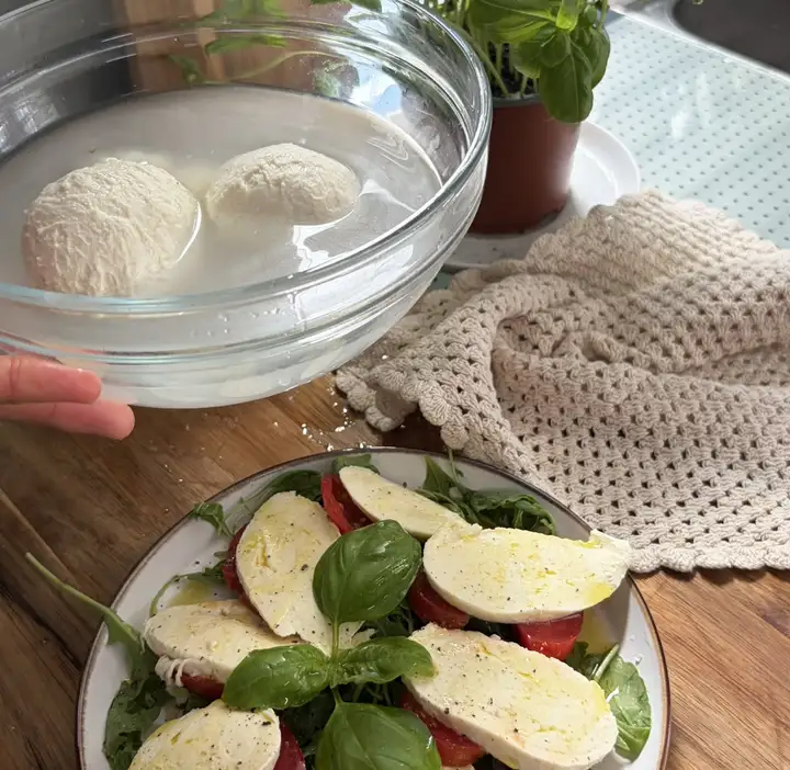 Selbstgezogene Mozzarella-Kugeln in eiskaltem Wasser und als Caprese angerichtet